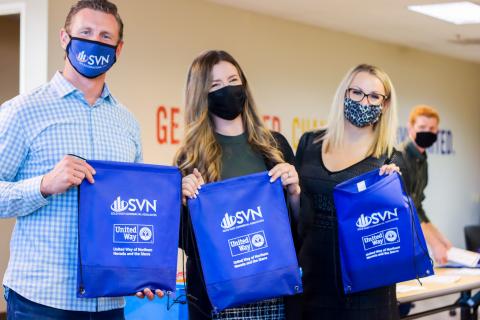 Volunteers from SVN holding up assembled book bags. 